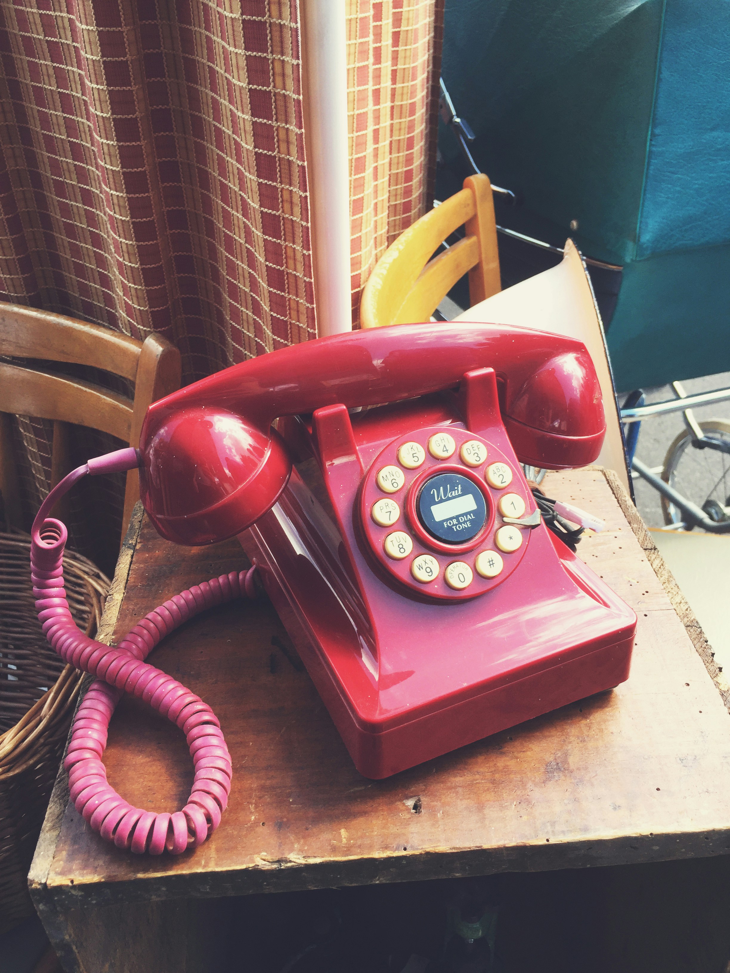 A red push-button desk telephone with a pink coiled cord, sitting on a wooden crate at a flea market